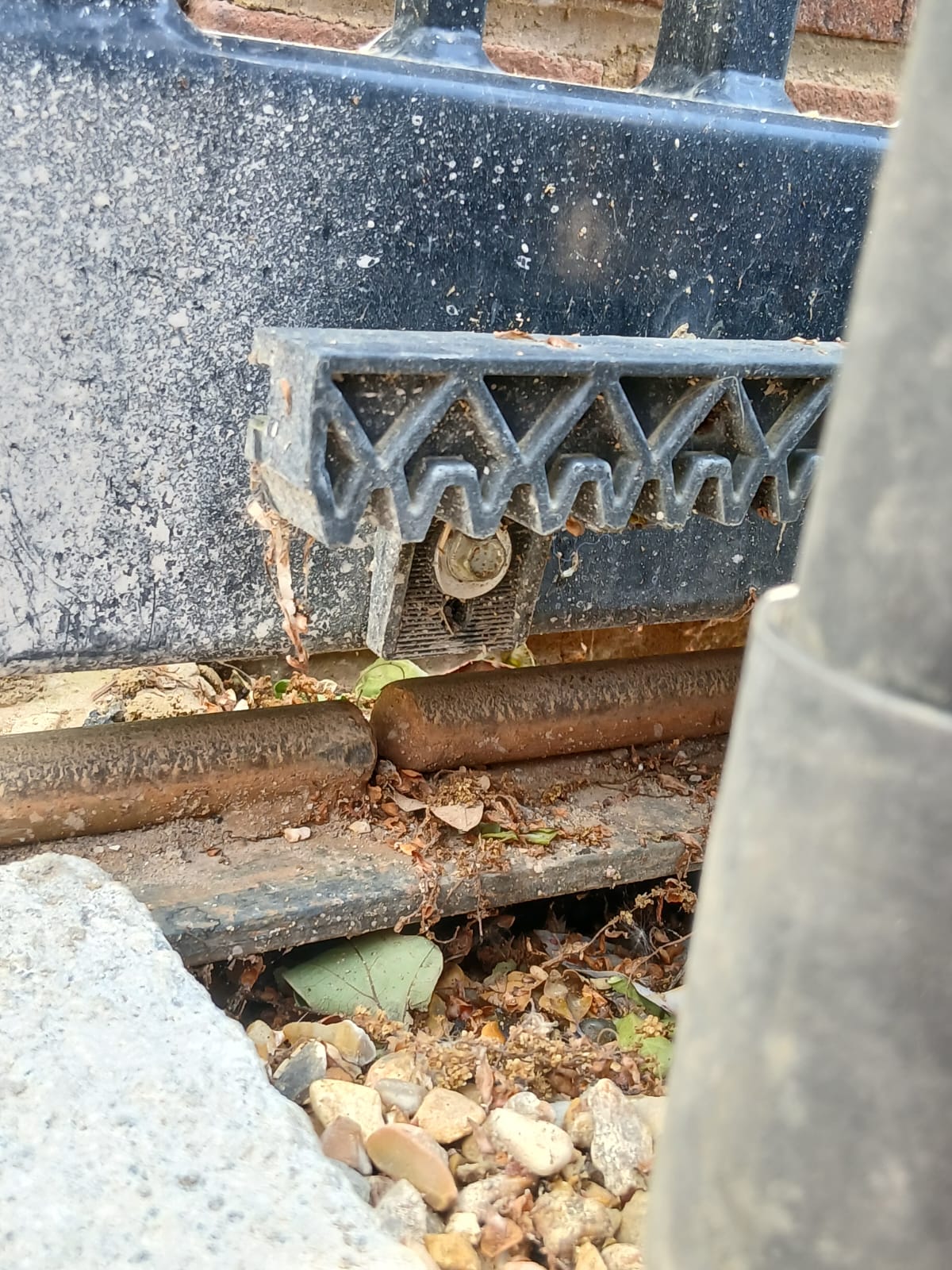 Sliding gate track with a visible gap and misalignment, debris between rails